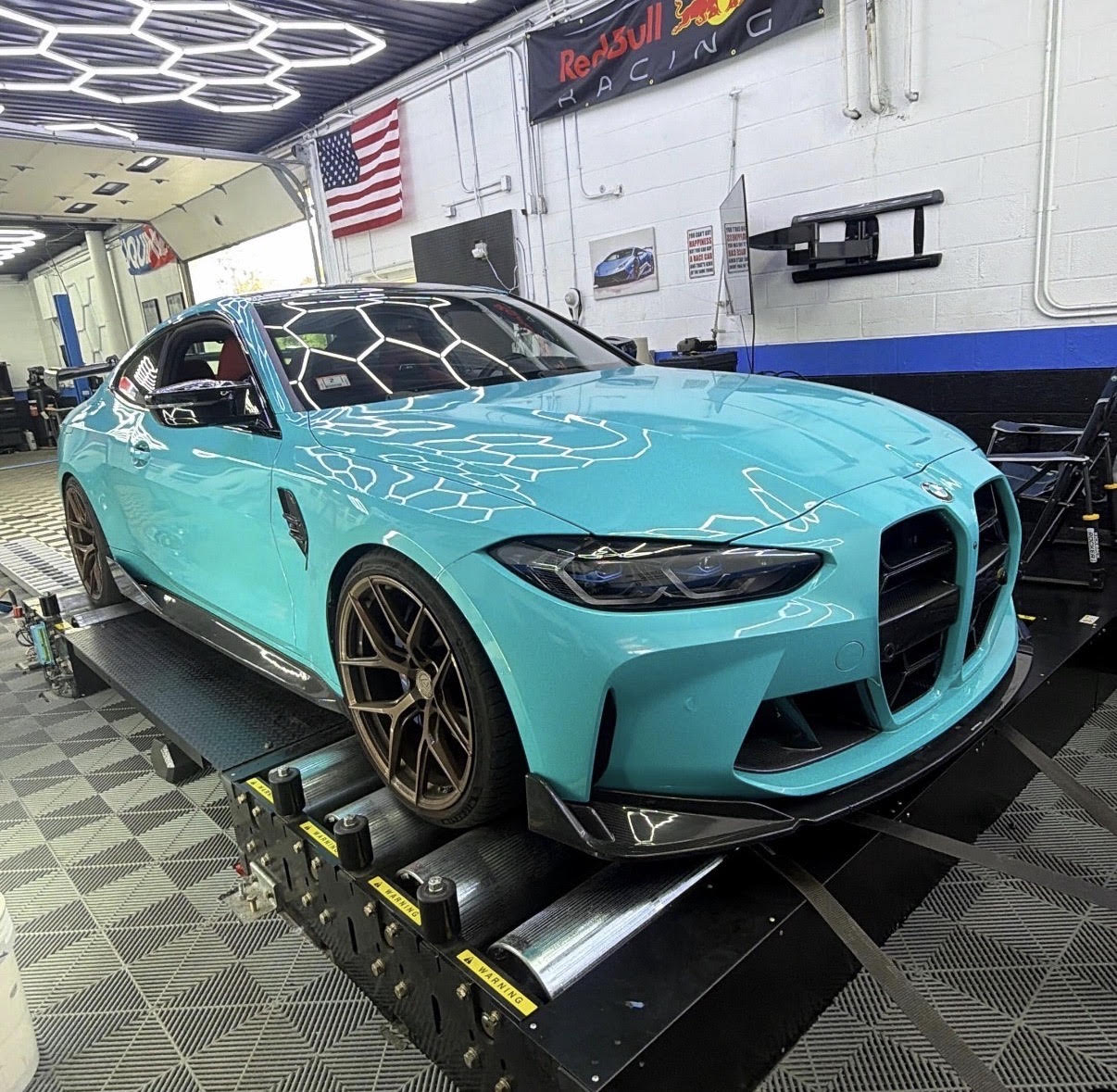 A teal BMW M4 strapped to the dyno